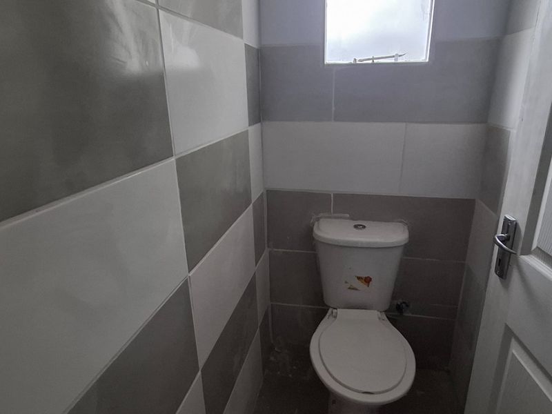 A small guest bathroom featuring two-tone wall tiling, a standard toilet, and an obscured glass window. The floor remains unfinished.