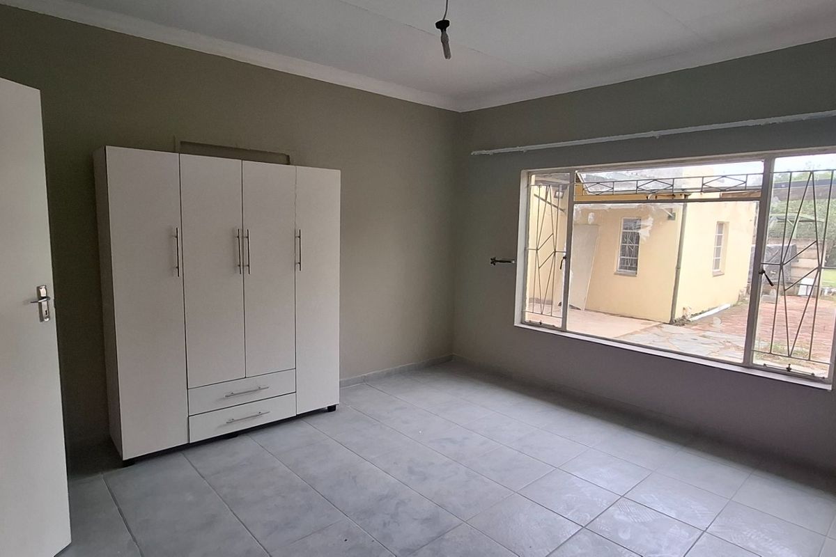 A spacious, empty bedroom featuring tiled flooring, a built-in wardrobe, and a large window with security bars, offering a neutral canvas for personalization.