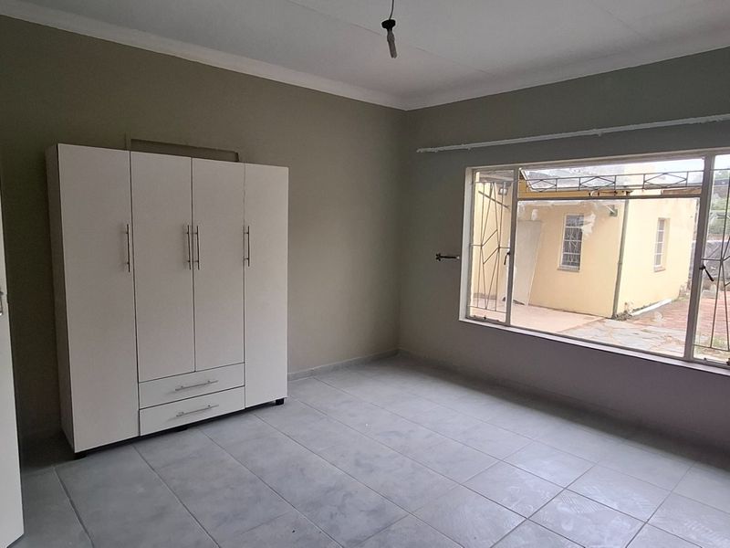 A spacious, empty bedroom featuring tiled flooring, a built-in wardrobe, and a large window with security bars, offering a neutral canvas for personalization.