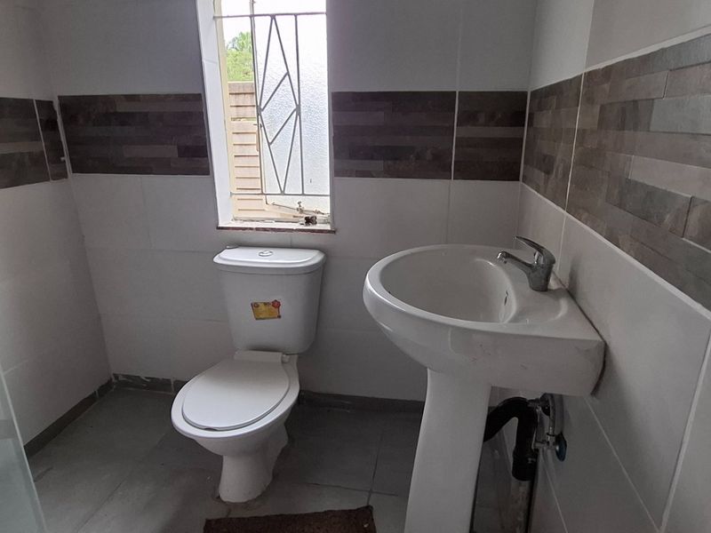 A functional bathroom featuring a pedestal basin, toilet, and shower enclosure with decorative tiled wall accents.