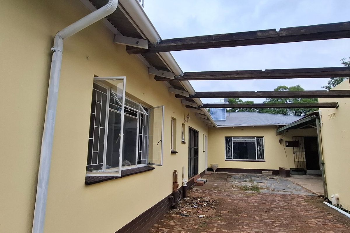 Rear exterior view of the property featuring a brick-paved courtyard, timber pergola structure, and steel-framed windows with security bars.