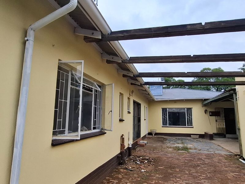 Rear exterior view of the property featuring a brick-paved courtyard, timber pergola structure, and steel-framed windows with security bars.