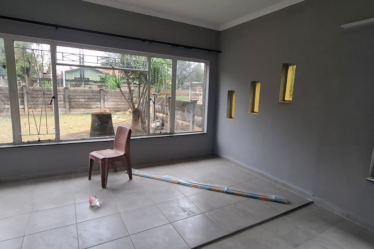 A bright, empty living room featuring large windows with security bars, tiled flooring, and unique decorative wall niches.