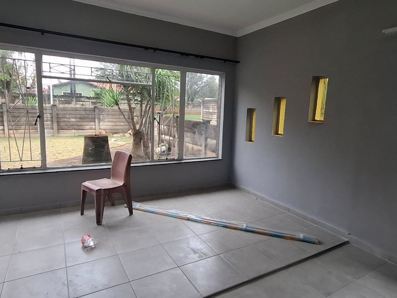 A bright, empty living room featuring large windows with security bars, tiled flooring, and unique decorative wall niches.