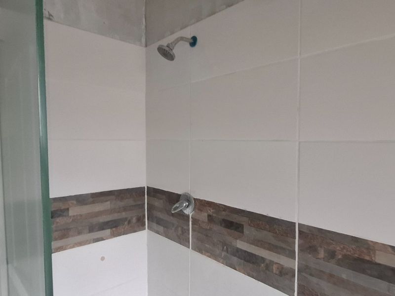 A bathroom shower enclosure featuring tiled walls with a decorative border and glass screen, currently requiring finishing work at the ceiling junction.