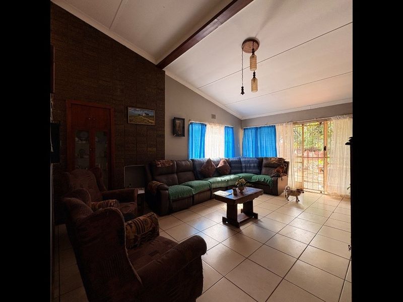 Spacious living room featuring a vaulted ceiling with exposed beam, tiled flooring, and a textured feature brick wall with access to the exterior.