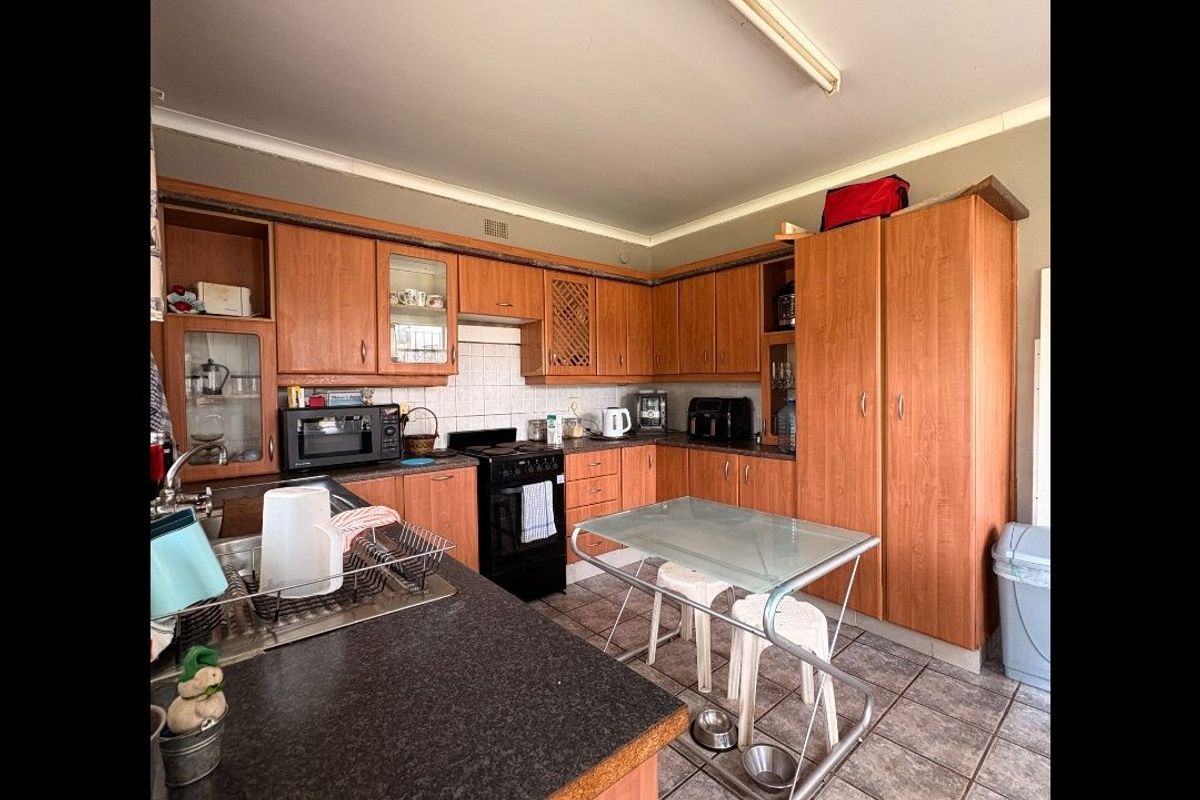 A functional kitchen featuring extensive wood-look cabinetry, laminate countertops, tiled backsplash, and tiled flooring, offering a practical layout with ample storage space.