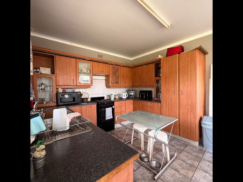 A functional kitchen featuring extensive wood-look cabinetry, laminate countertops, tiled backsplash, and tiled flooring, offering a practical layout with ample storage space.