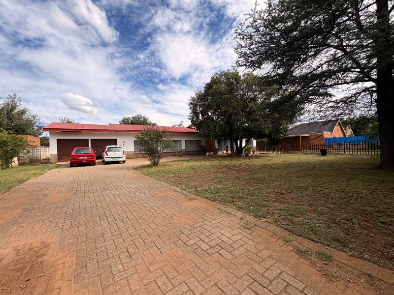 Front view of a single-story house featuring a paved driveway, double garage, and a spacious front garden with mature trees.