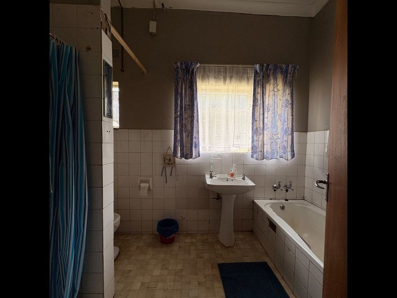 A dated bathroom featuring a pedestal basin, built-in bathtub, and tiled wall finishes, requiring modernization and cosmetic updates.