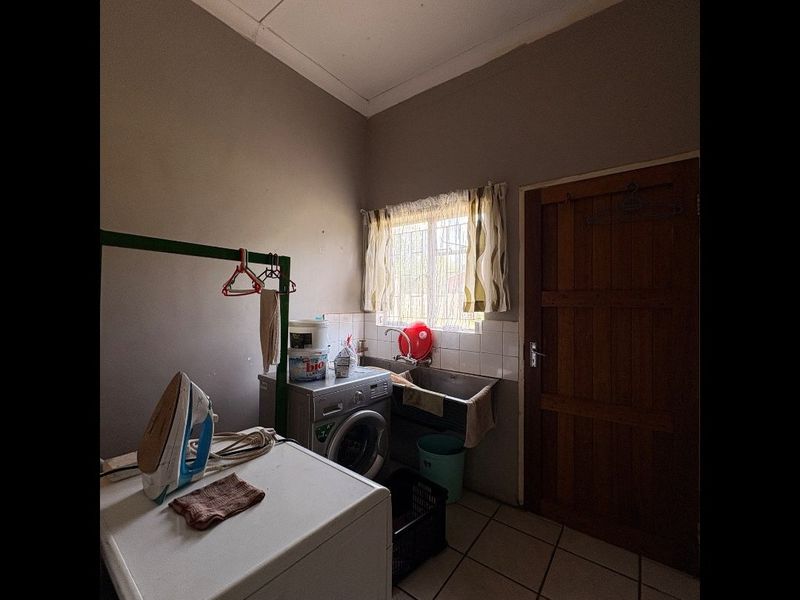 A functional laundry room featuring a stainless steel sink, tiled splashback, and tiled flooring, providing a practical space for household utility tasks.