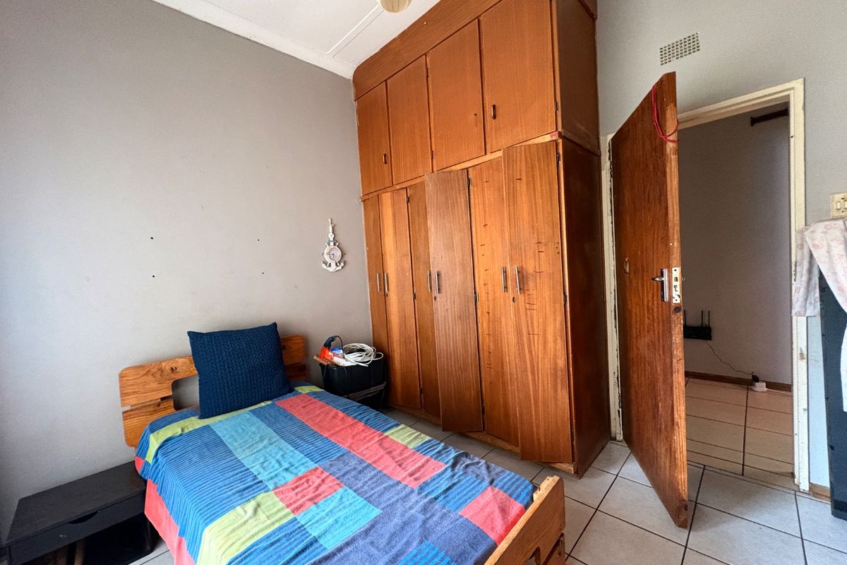 A bedroom featuring built-in wooden cupboards, tiled flooring, and a standard ceiling light fixture.