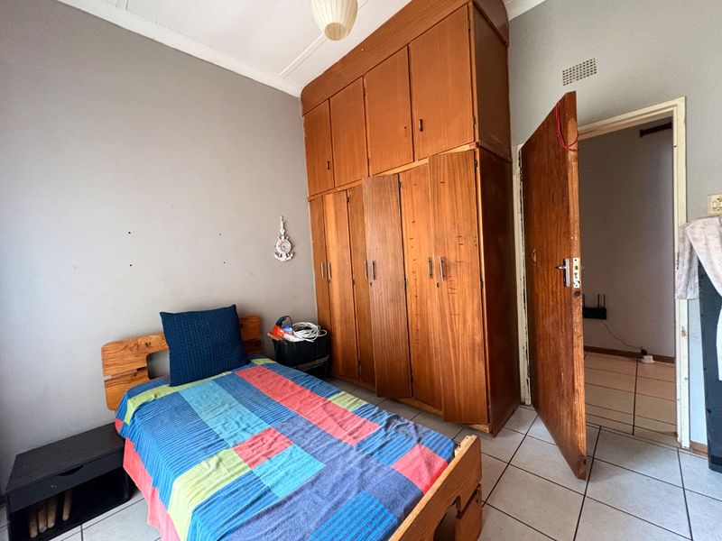 A bedroom featuring built-in wooden cupboards, tiled flooring, and a standard ceiling light fixture.