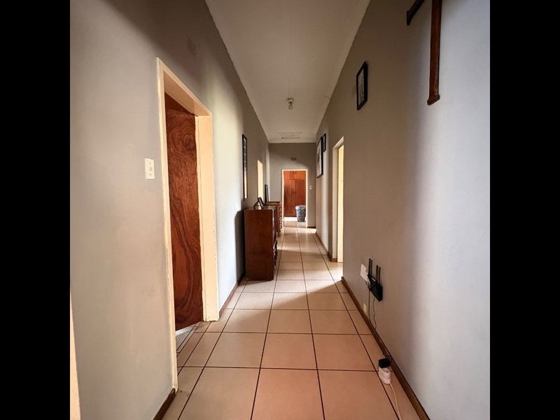A functional residential hallway featuring tiled flooring and multiple wooden door frames leading to various rooms.