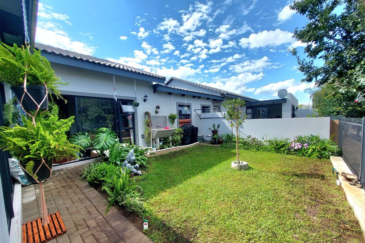 A well-maintained rear garden featuring a paved walkway, manicured lawn, boundary wall, and direct access to the home via sliding glass doors.