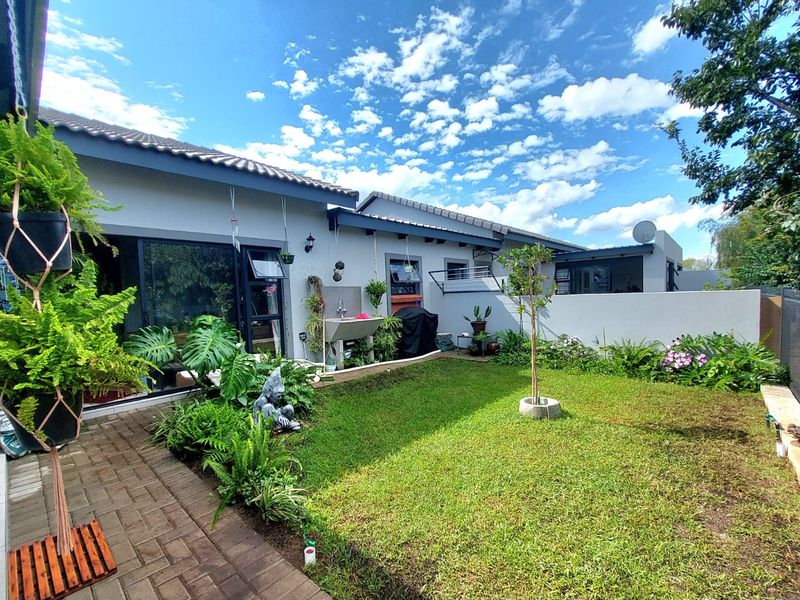 A well-maintained rear garden featuring a paved walkway, manicured lawn, boundary wall, and direct access to the home via sliding glass doors.