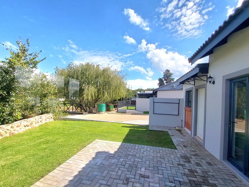 A well-maintained rear exterior featuring a paved patio area, manicured lawn, and stone retaining wall, providing a clean and inviting outdoor space.
