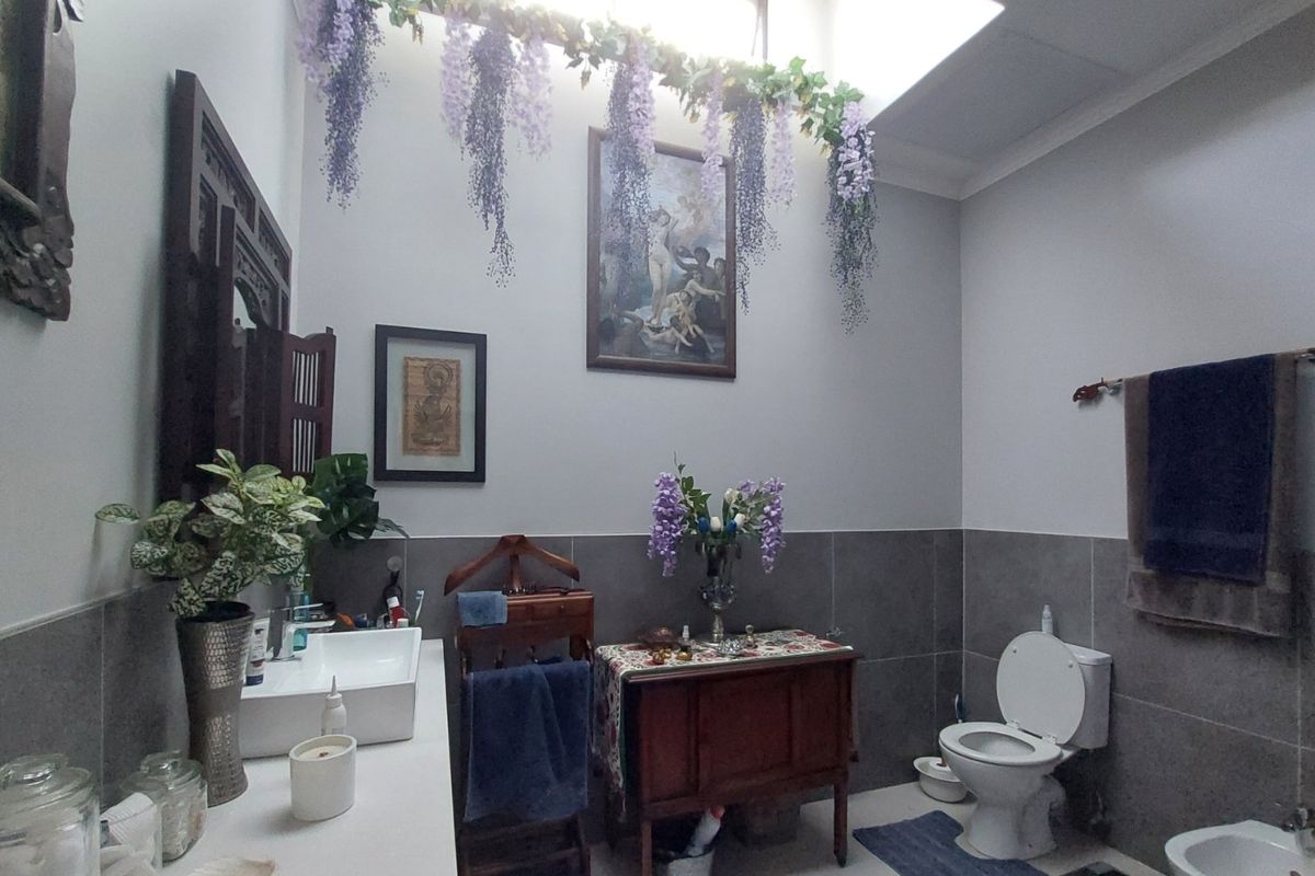 A well-lit bathroom featuring a vessel sink, toilet, bidet, and modern grey wall tiling, enhanced by a natural light-filled skylight.