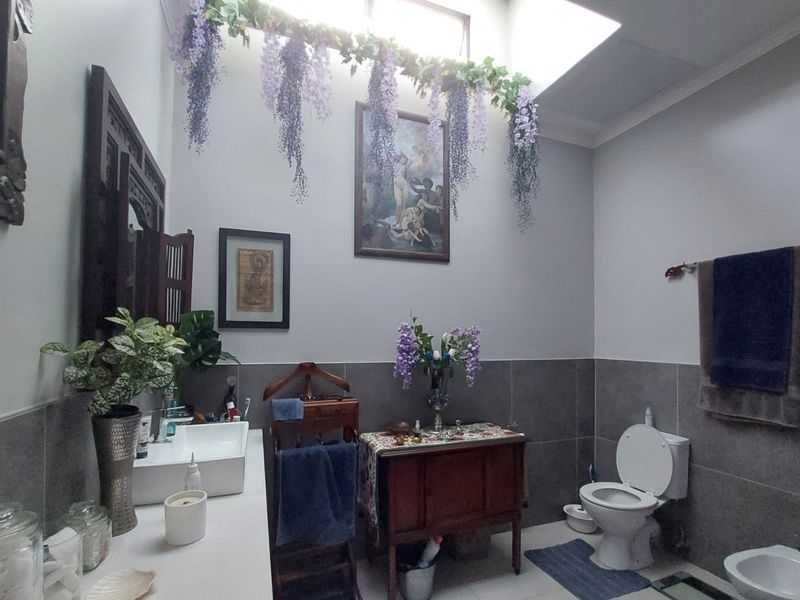 A well-lit bathroom featuring a vessel sink, toilet, bidet, and modern grey wall tiling, enhanced by a natural light-filled skylight.