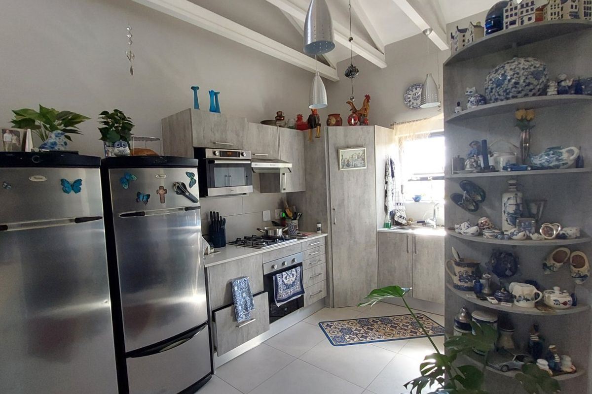 A functional kitchen featuring modern grey cabinetry, built-in appliances, tiled flooring, and high ceilings with exposed rafters, offering a bright and practical workspace.