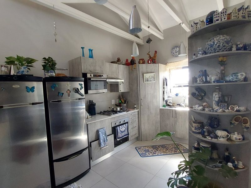 A functional kitchen featuring modern grey cabinetry, built-in appliances, tiled flooring, and high ceilings with exposed rafters, offering a bright and practical workspace.