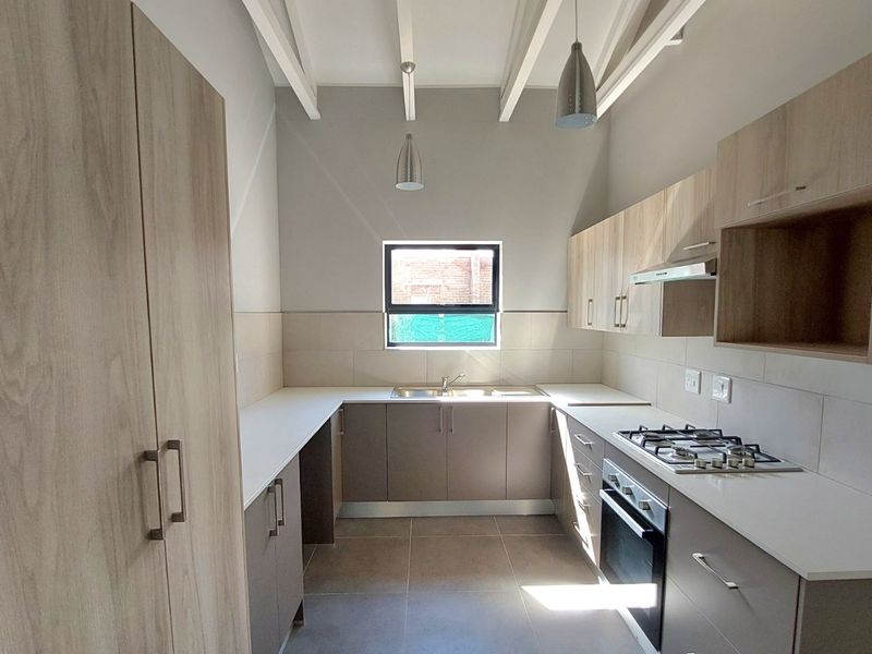 Modern kitchen featuring light wood-tone cabinetry, stone countertops, gas hob, built-in oven, and exposed ceiling beams in a clean, contemporary layout.