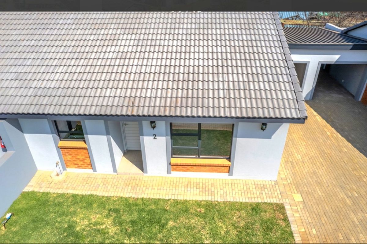 Aerial view of the townhouse exterior featuring a tiled roof, paved driveway, and neat front garden area.