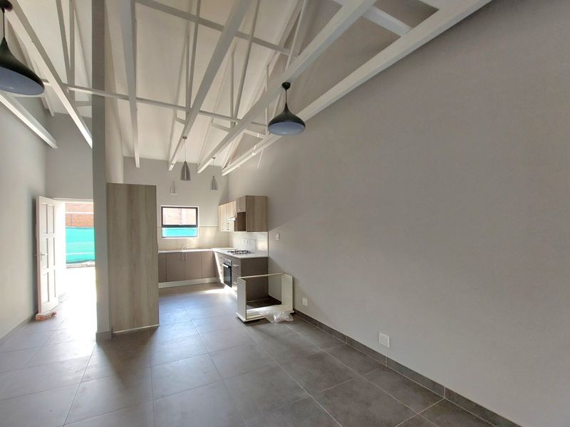 Open-plan living area featuring high ceilings with exposed trusses, tiled flooring, and a modern kitchen with built-in cabinetry and integrated appliances.