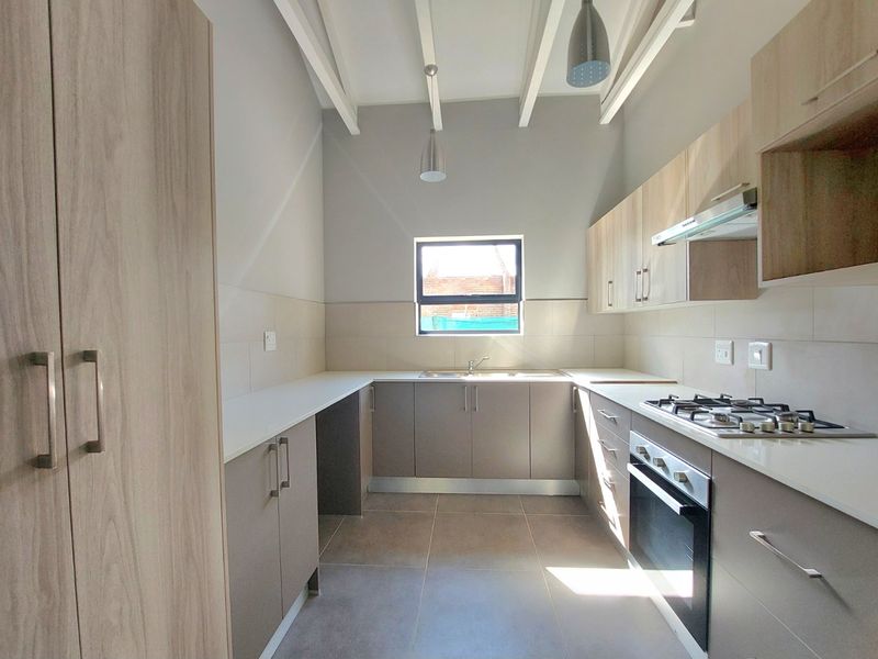 A modern, well-lit kitchen featuring light wood-tone cabinetry, a gas hob, built-in oven, and tiled finishes with exposed ceiling beams.