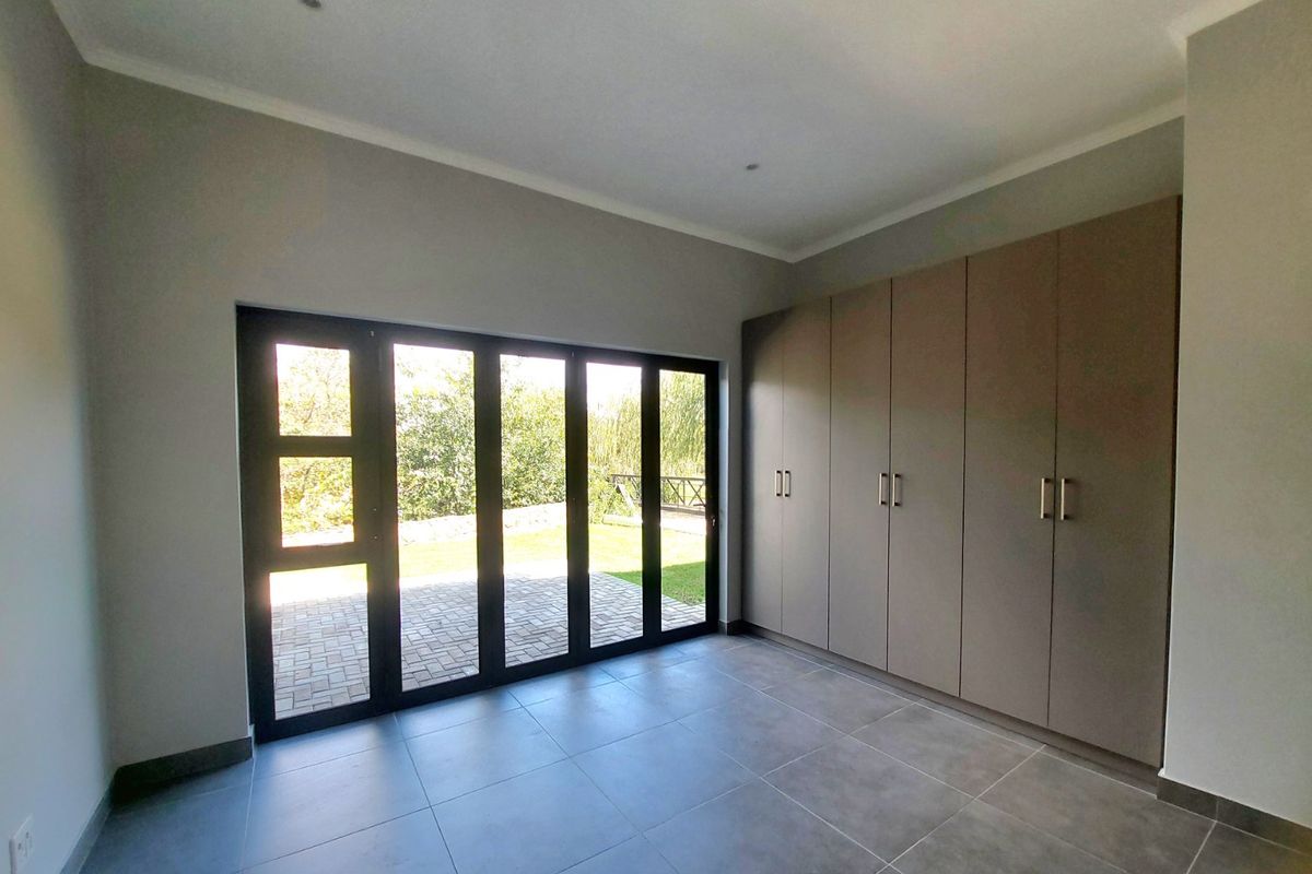 A bright, modern bedroom featuring neutral tiled flooring, extensive built-in cupboards, and large aluminium stacker doors opening onto a paved patio area.