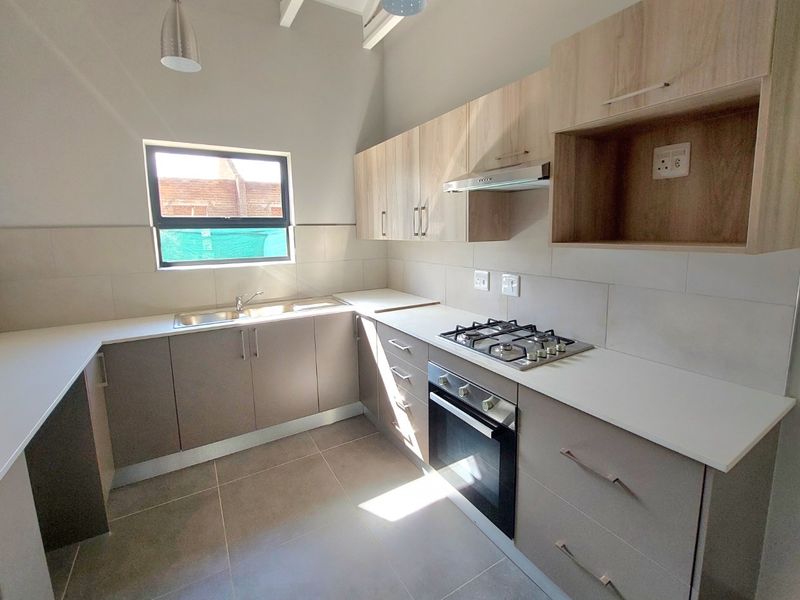 Modern kitchen featuring light wood-tone cabinetry, gas hob, built-in oven, extractor fan, and neutral tiled finishes with exposed ceiling beams.