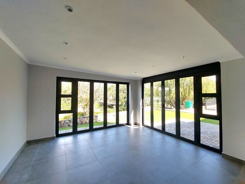 Spacious, light-filled living area featuring modern grey floor tiles and expansive black aluminium stacker doors opening onto the garden.