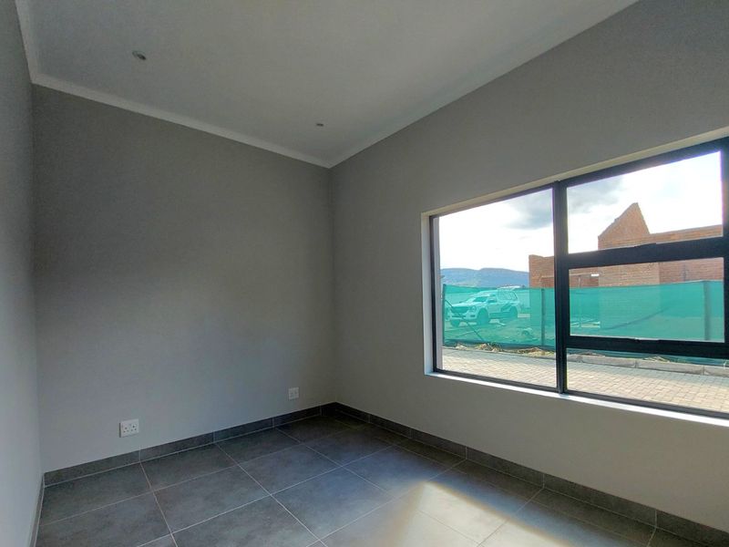A clean, modern, and empty bedroom featuring neutral grey walls, large aluminium-framed windows, and contemporary tiled flooring.
