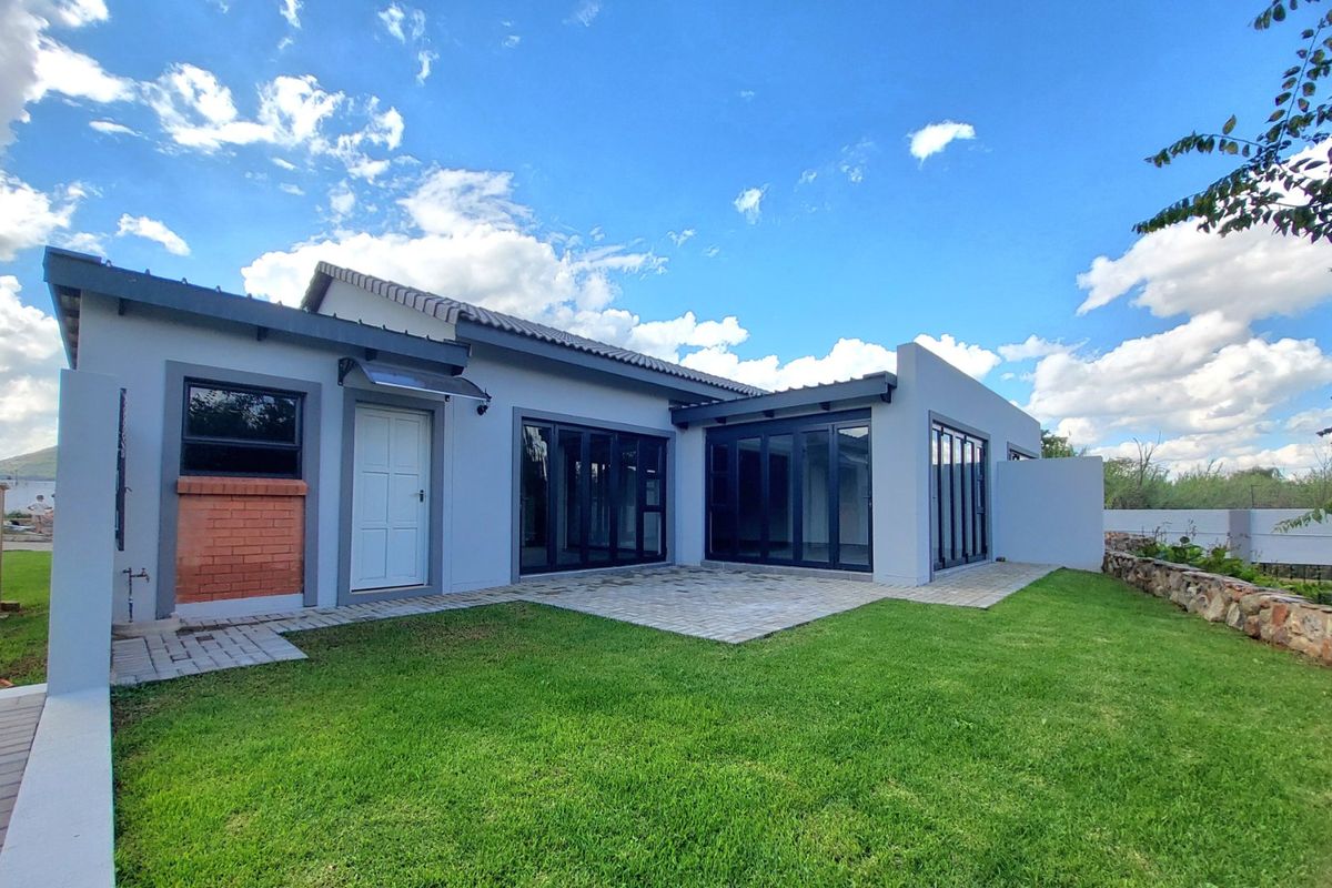 Rear view of the townhouse featuring a paved patio, modern bi-fold doors, and a well-maintained garden with a stone retaining wall.