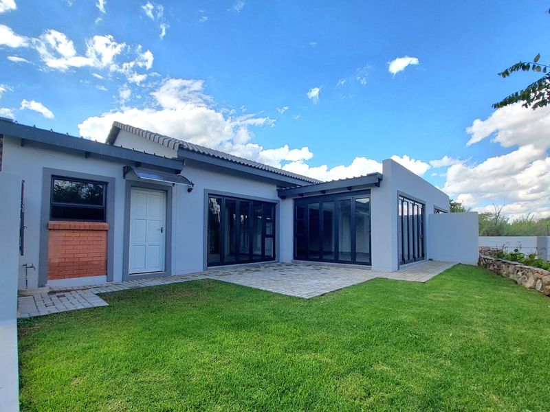 Rear view of the townhouse featuring a paved patio, modern bi-fold doors, and a well-maintained garden with a stone retaining wall.