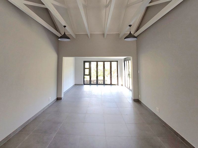 Spacious open-plan living area featuring high ceilings with exposed timber beams, neutral tiled flooring, and large folding doors providing ample natural light.