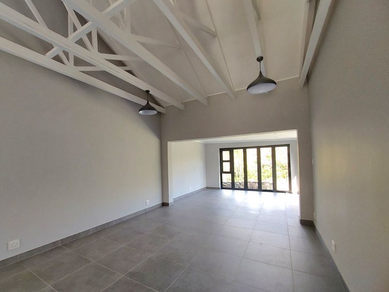 Spacious open-plan living area featuring high ceilings with exposed white trusses, modern tiled flooring, and large sliding glass doors leading to the outdoors.