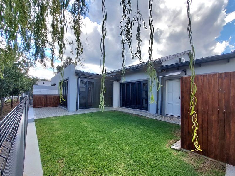 A well-maintained rear garden featuring a paved patio area, lush lawn, and modern black aluminium sliding doors leading into the townhouse.