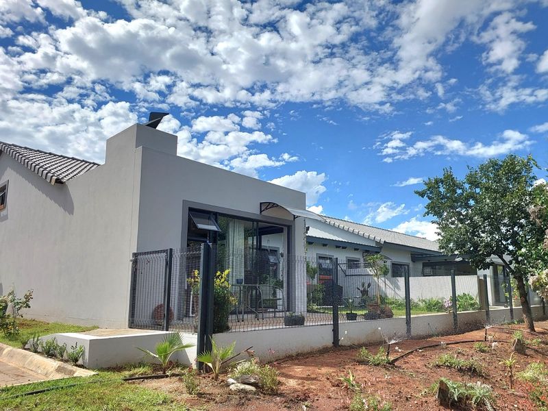 Rear view of the townhouse featuring a paved patio area, sliding glass doors, and a fenced garden space under a clear blue sky.