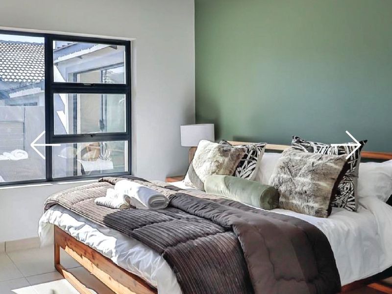 A well-maintained bedroom featuring a modern green accent wall, tiled flooring, and large aluminium-framed windows allowing for natural light.