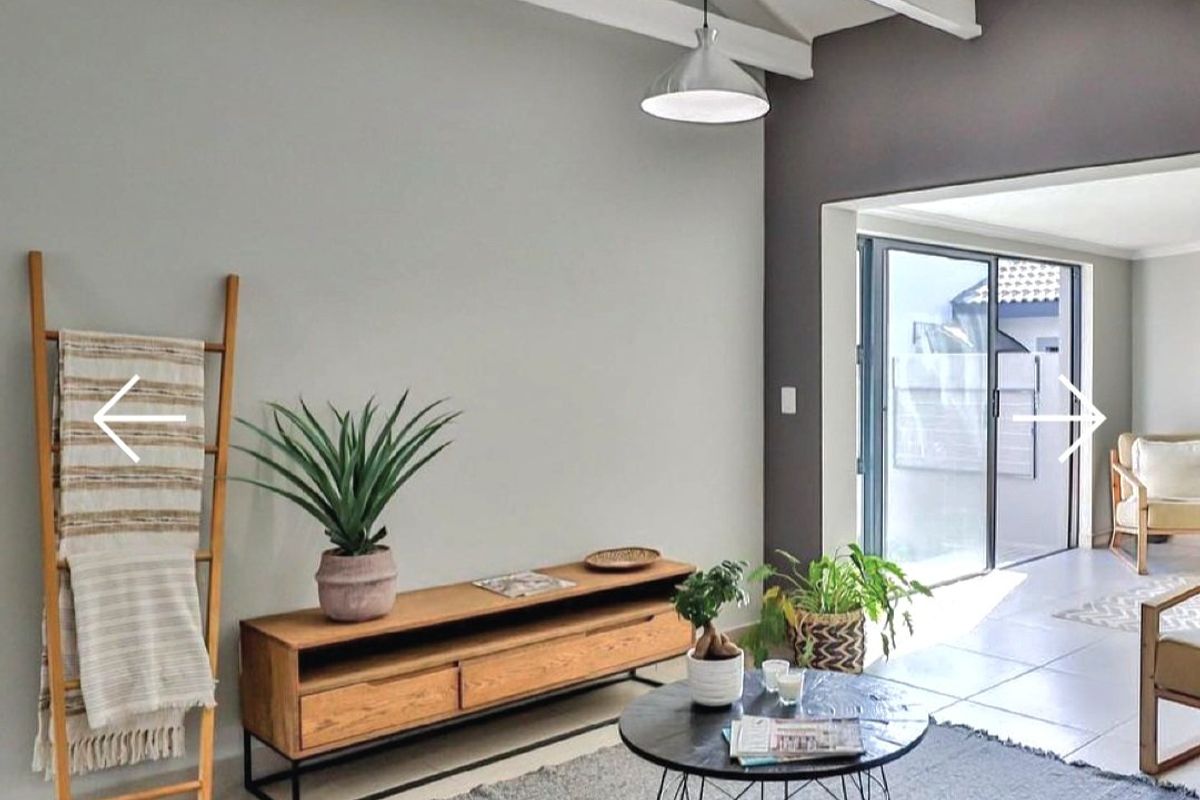 A bright living room featuring exposed white timber ceiling beams, tiled flooring, and large sliding glass doors providing access to an outdoor patio area.