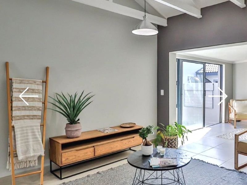 A bright living room featuring exposed white timber ceiling beams, tiled flooring, and large sliding glass doors providing access to an outdoor patio area.