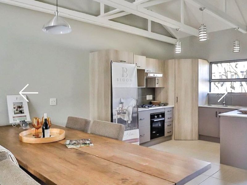 Open-plan living and kitchen area featuring exposed white roof trusses, modern cabinetry, built-in appliances, and tiled flooring throughout.