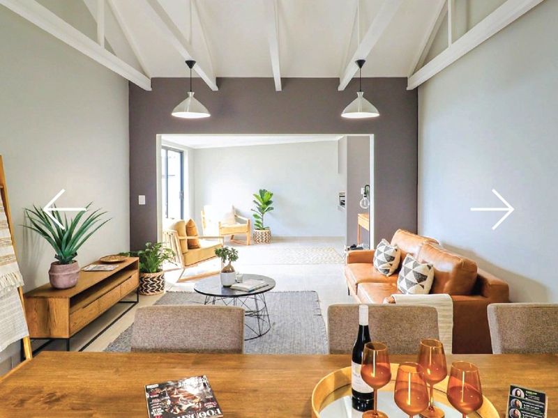Spacious open-plan living and dining area featuring high vaulted ceilings with exposed white timber beams and modern pendant lighting.