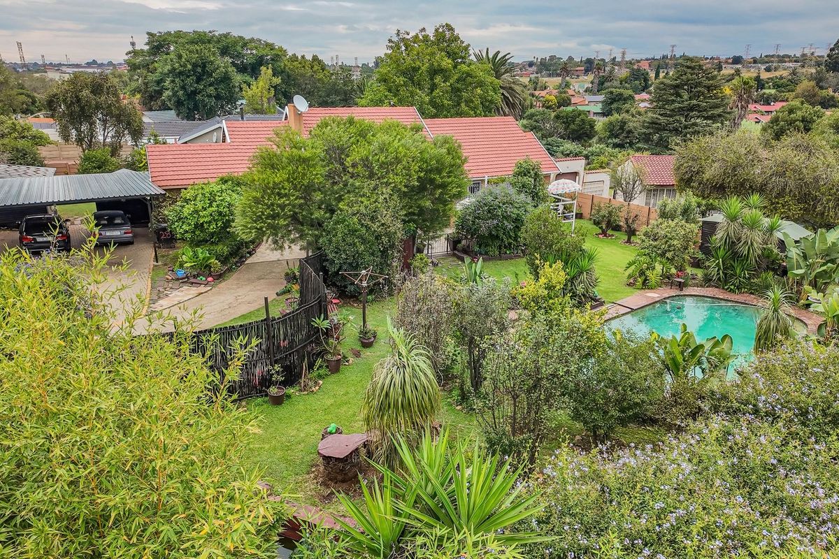 Aerial view of a residential property featuring a swimming pool, established garden, paved driveway, and a covered carport.
