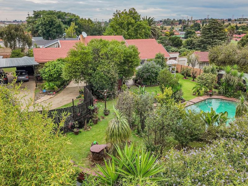 Aerial view of a residential property featuring a swimming pool, established garden, paved driveway, and a covered carport.
