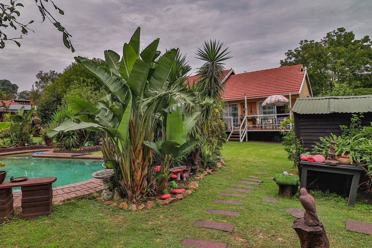 Rear garden view featuring a swimming pool with brick coping, a raised wooden deck attached to the house, and a well-established lawn area.