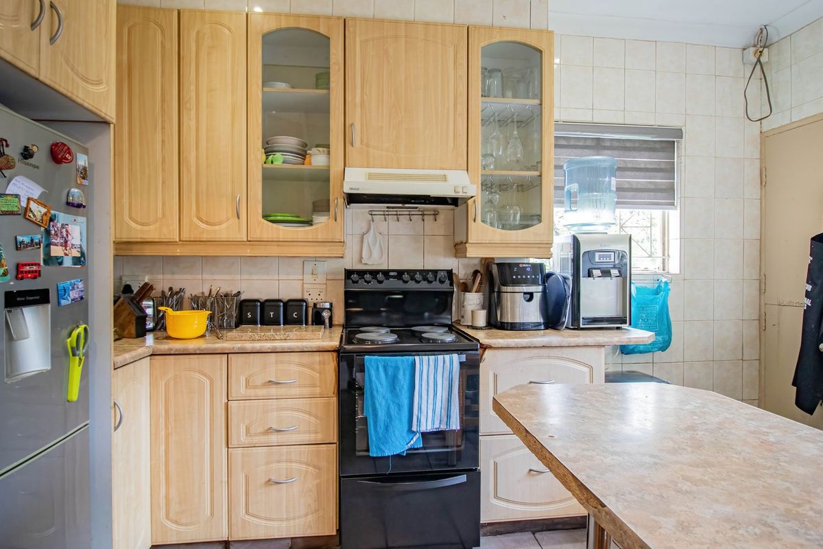 A functional kitchen featuring light wood-tone cabinetry, laminate countertops, a tiled backsplash, and a freestanding electric stove with an integrated extractor fan.