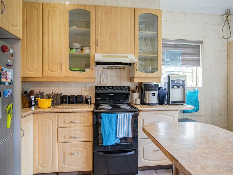 A functional kitchen featuring light wood-tone cabinetry, laminate countertops, a tiled backsplash, and a freestanding electric stove with an integrated extractor fan.