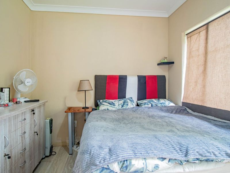 A functional bedroom featuring neutral wall tones, laminate flooring, and a window with fitted blinds.